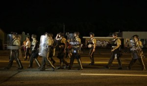 Police walk around protesters as people gather along West Florissant Avenue in Ferguson, Mo., Tuesday, Aug. 11, 2015. The St. Louis suburb has seen demonstrations for days marking the anniversary of the death of 18-year-old Michael Brown, whose shooting death by a Ferguson police officer sparked a national "Black Lives Matter" movement. Tuesday was the fifth consecutive night a crowd gathered on West Florissant, the thoroughfare that was the site of massive protests and rioting after Brown was killed. (AP Photo/Jeff Roberson)
