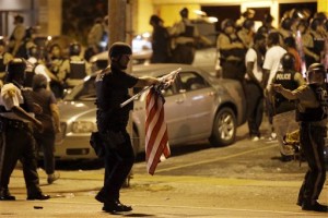 An officer holds a flag he took from a protestor, Monday, Aug. 10, 2015, in Ferguson, Mo. Ferguson was a community on edge again Monday, a day after a protest marking the anniversary of Michael Brown's death was punctuated with gunshots. (AP Photo/Jeff Roberson)