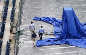 Men walk on the tarp-covered court in Arthur Ashe Stadium after the women's semifinal matches were postponed until Friday because of rain at the U.S. Open tennis tournament in New York, Thursday, Sept. 10, 2015. (AP Photo/Kathy Willens)