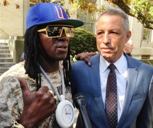 Entertainer Flavor Flav, left, standing with attorney Todd Greenberg, speaks with reporters after pleading guilty to one count of aggravated unlicensed operation of a motor vehicle, Tuesday, Oct. 13, 2015, in Mineola, N.Y. Flav, whose real name is William Drayton, Jr., was arrested in January, 2014 while racing to his mother's funeral on Long Island. A judge in Nassau Criminal Court on Tuesday sentenced Flav to time served, essentially the time he was in custody following the arrest. He was fined $3,600. (AP Photo/Frank Eltman)