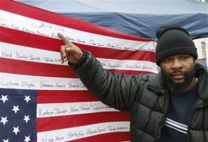 Jamine Clark points to the name of his brother, Jamar Clark, on an upside-down flag bearing names of people killed at the hands of police outside the Minneapolis Police Department's Fourth Precinct, Tuesday, Nov. 17, 2015, in Minneapolis. Black Lives Matter demonstrators have set up an encampment at the precinct which is near the site of the Sunday shooting of Jamar Clark by a Minneapolis police officer.  Clark has been taken off life support. (AP Photo/Jim Mone)