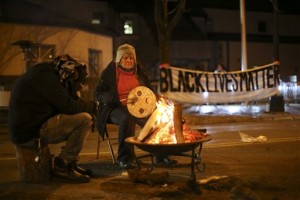 People warm themselves as they demonstrate since the Nov. 10 shooting of 24-year-old Jamar Clark, in front of the Minneapolis Police 4th Precinct on Tuesday, Nov. 24, 2015. Minneapolis police were searching Tuesday for three white males suspected of shooting at five Black Lives Matter demonstrators, while the family of a black man who was fatally shot by a city police officer called for the dayslong protests outside of the police precinct to end. (Jeff Wheeler/Star Tribune via AP)