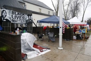 Members of Black Lives Matter continue their encampment, Tuesday, Nov. 17, 2015, outside the Minneapolis Police Department's Fourth Precinct. Protesters said they would continue the precinct sit-in until authorities release any video they have of the incident as well as the officer's identity. Clark has been removed from life support. (AP Photo/Jim Mone)