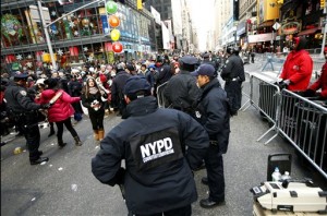 In this Dec. 31, 2104 file photo, counterterrorism officers, foreground, armed with an explosives detection device, far right, watch as other police officers inspect revelers entering a cordoned off area in Times Square in New York, on New Years Eve. On Tuesday, Dec. 29, 2015 New York City officials sought to assure potential revelers that Times Square will be one the safest places in the world on New Years Eve.   (AP Photo/Kathy Willens, File)