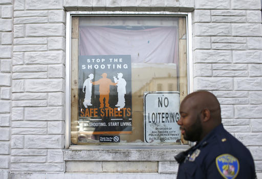 In this March 31, 2016 photo, Baltimore Police Department Officer Jordan Distance walks past signs in a row home's window during a foot patrol in Baltimore. In the year since Freddie Gray died, the Baltimore police department has worked on its relationship with the community and tried to heal wounds opened during protests and rioting last spring.  Part of the departments efforts have been putting more officers on foot patrol in poor, mostly black neighborhoods and encouraging beat cops to get more involved in the community.  (AP Photo/Patrick Semansky)
