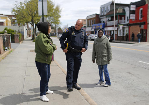 In this April 8, 2016 photo, Baltimore Police Department Officer Ken Hurst, center, chats with residents as he walks a foot patrol in Baltimore. Hurst is one of 450 police officers who are part of a foot patrol program aimed at getting officers out of their cars and onto the streets of the city's most dangerous neighborhoods, not to make arrests but to make friends. (AP Photo/Patrick Semansky)